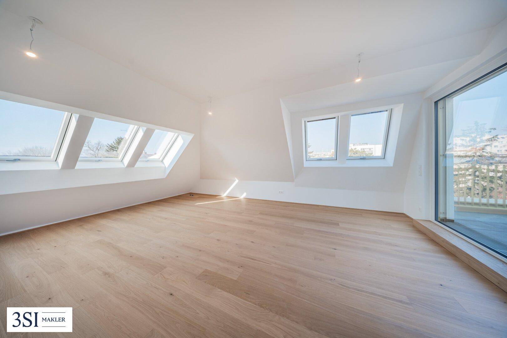 Lichtdurchfluteter Raum im Dachgeschoss mit Holzboden und mehreren Dachfenstern.