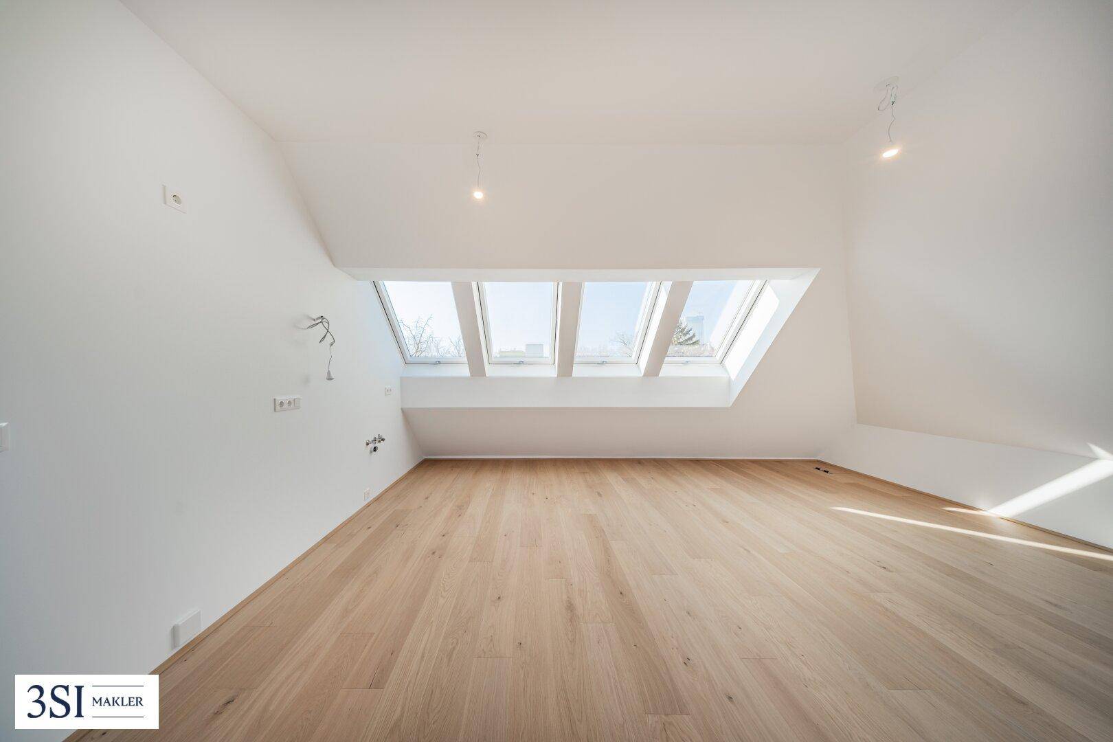 Geräumiges Dachgeschosszimmer mit schrägen Wänden, Holzboden und großen Dachfenstern.