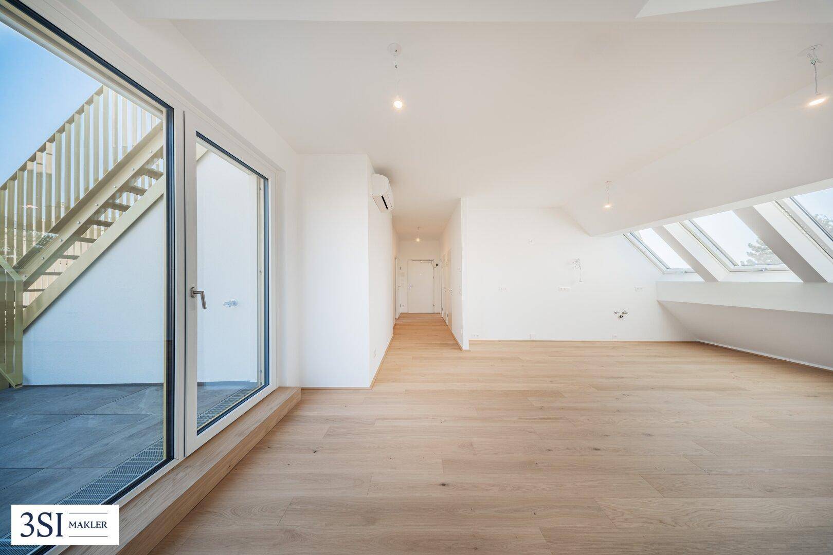 Helles Dachgeschosszimmer mit Holzboden, großen Fenstern und Zugang zu einer Außenterrasse.