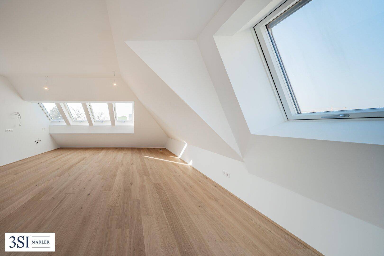Geräumiges Dachgeschosszimmer mit Holzboden und schrägen Dachfenstern, die viel Licht spenden.