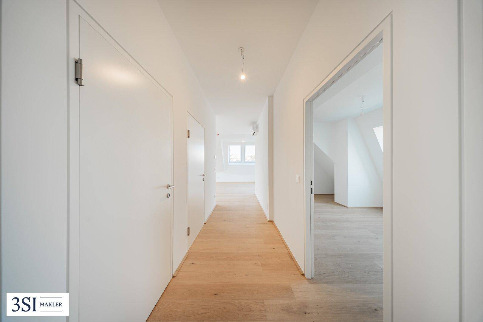 Heller Flur mit Holzboden und weißen Türen, der zu weiteren Räumen führt.