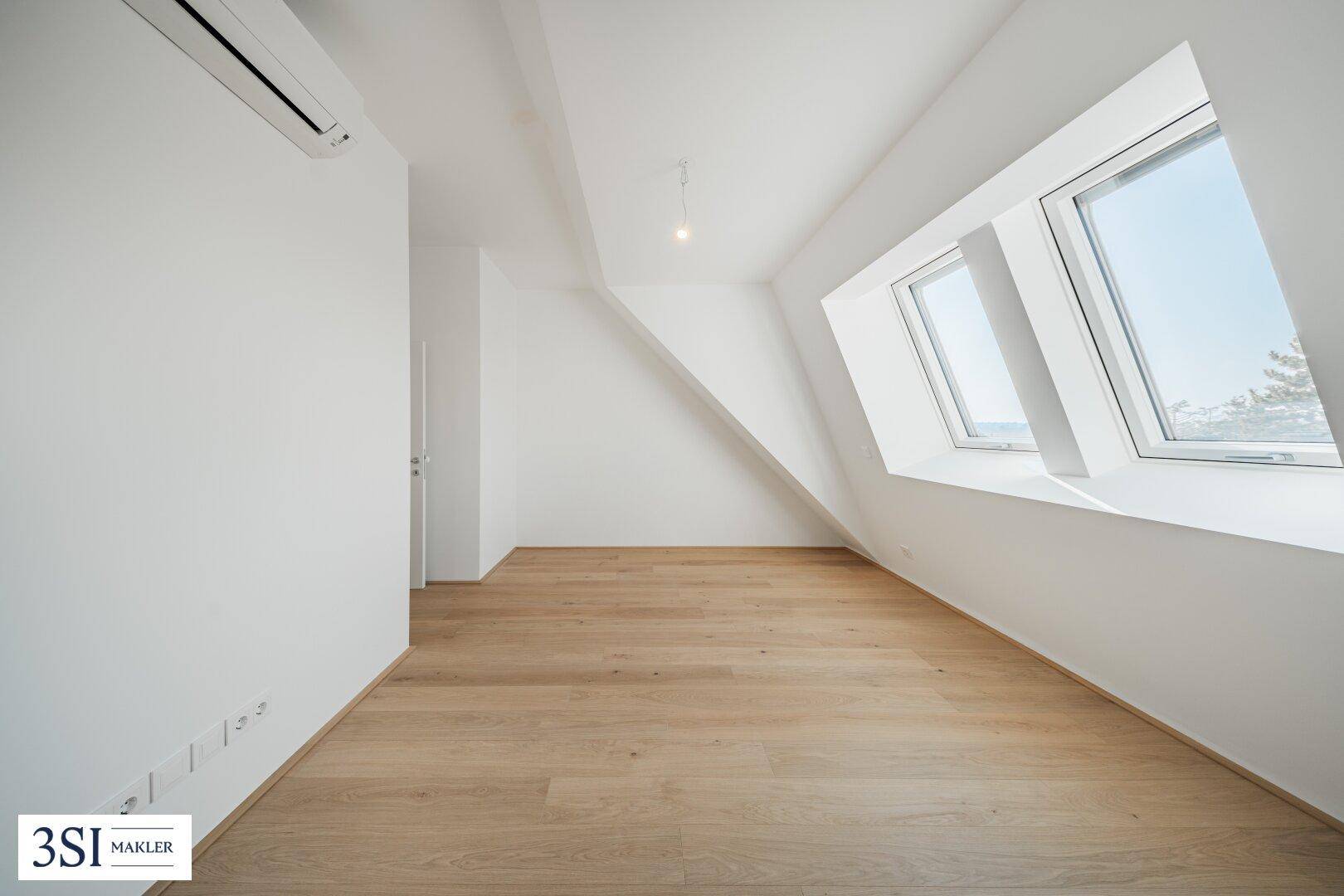 Geräumiges Dachgeschosszimmer mit Holzboden, Klimaanlage und schrägen Dachfenstern.