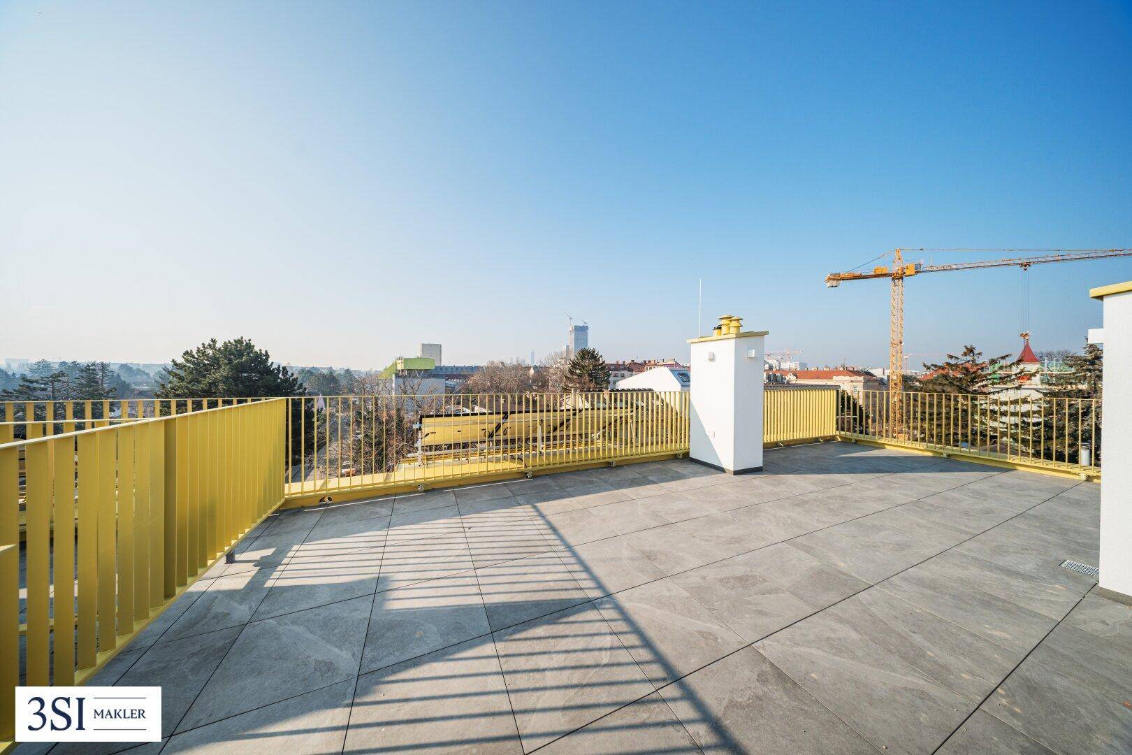 Weitläufige Dachterrasse mit Panoramablick über die Stadt und gelbem Sicherheitsgeländer.