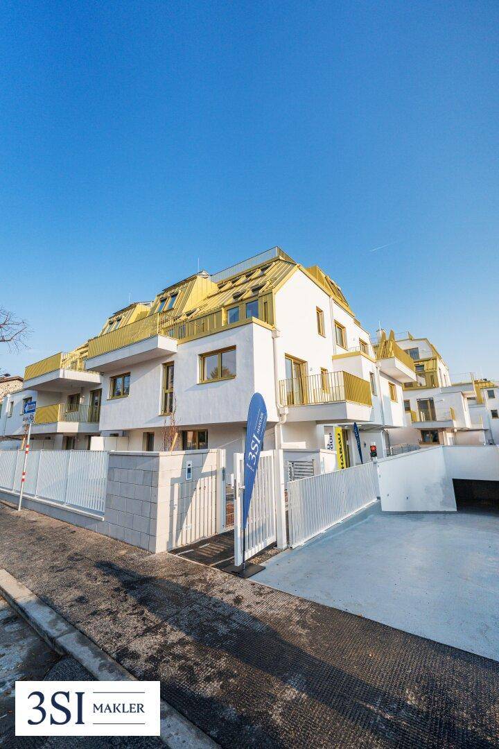Moderne Wohnanlage mit weißer Fassade, gelben Balkonen und Tiefgaragenzufahrt.