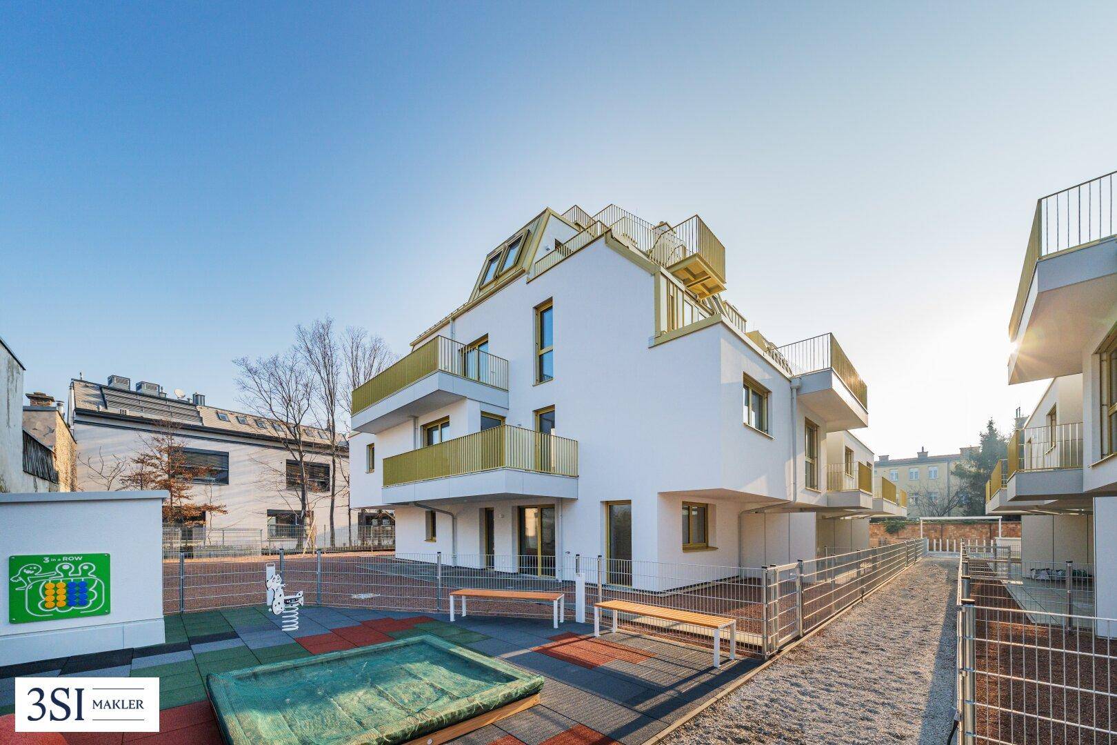Neubau-Wohnanlage mit Spielplatz und modernen Balkonen in einer grünen Umgebung.