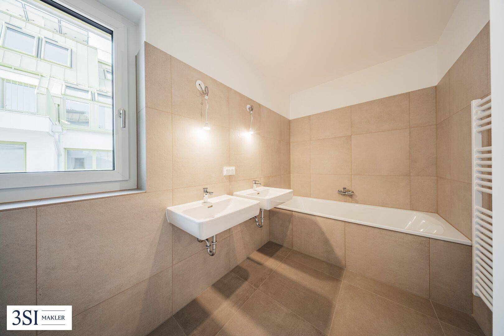 Modernes Badezimmer mit zwei Waschbecken, Badewanne und beigefarbenen Fliesen.
