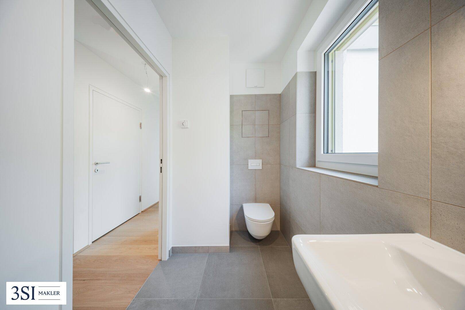 Separates Gäste-WC mit modernem Wand-WC, Waschbecken und grauen Fliesen.