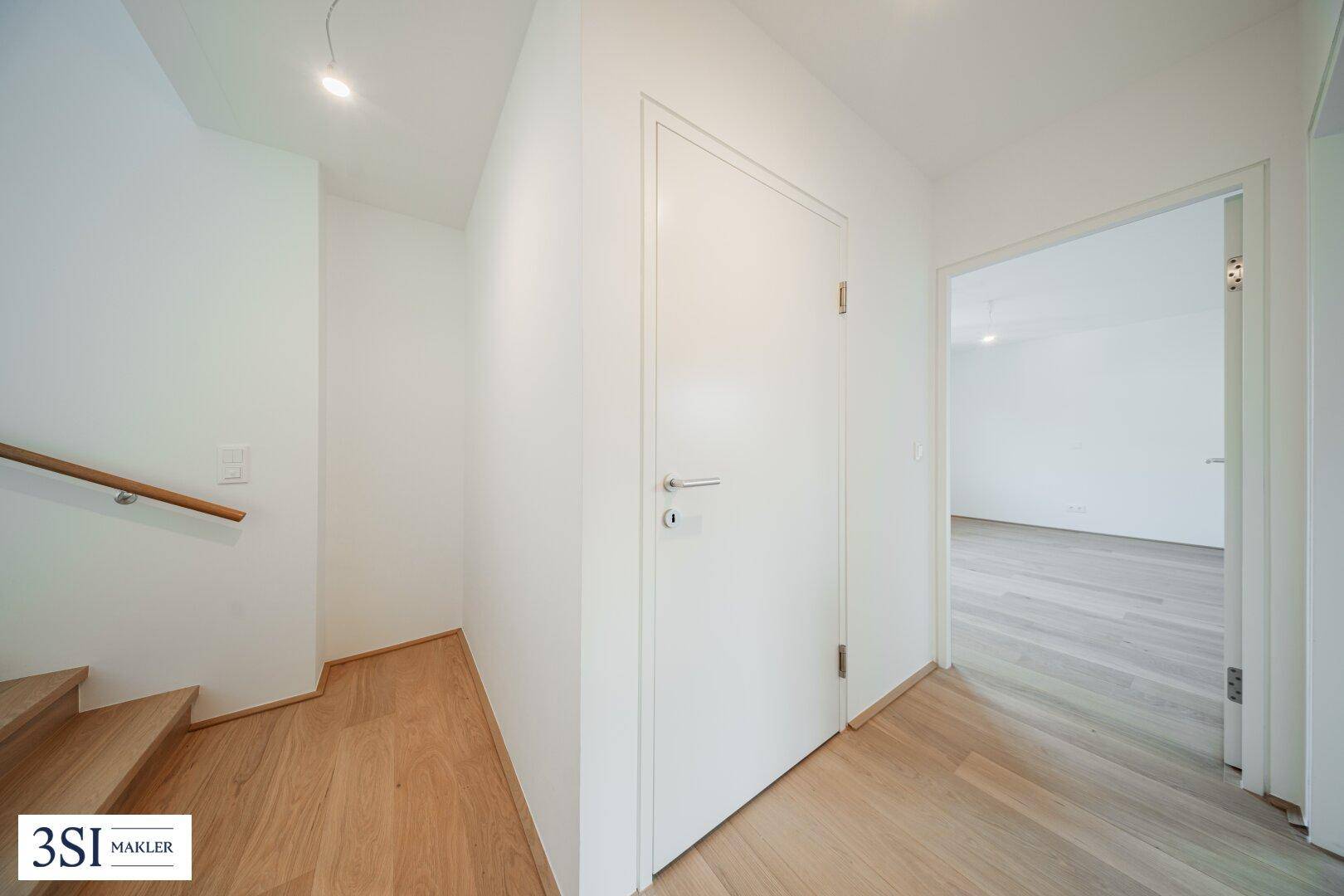 Heller Flur mit Holztreppe und Holzboden, der zu weiteren Räumen führt.
