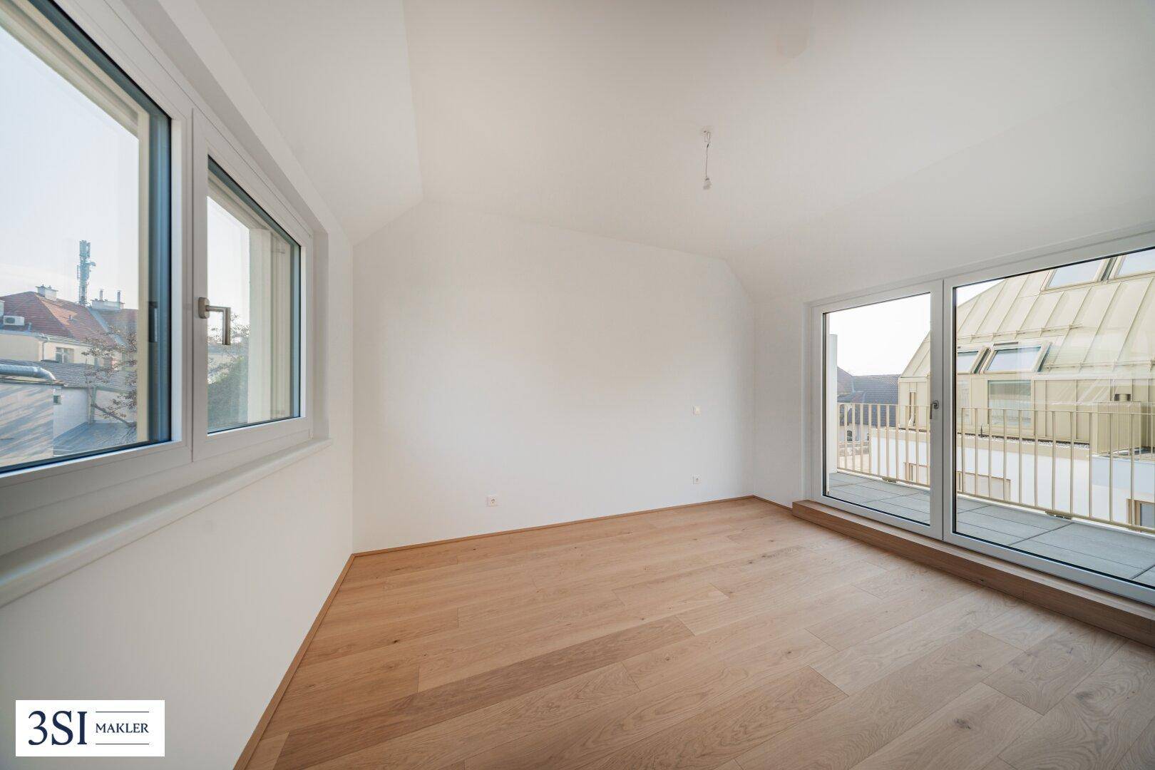 Helles Zimmer mit Holzboden und Zugang zu einem Balkon mit Blick nach draußen.