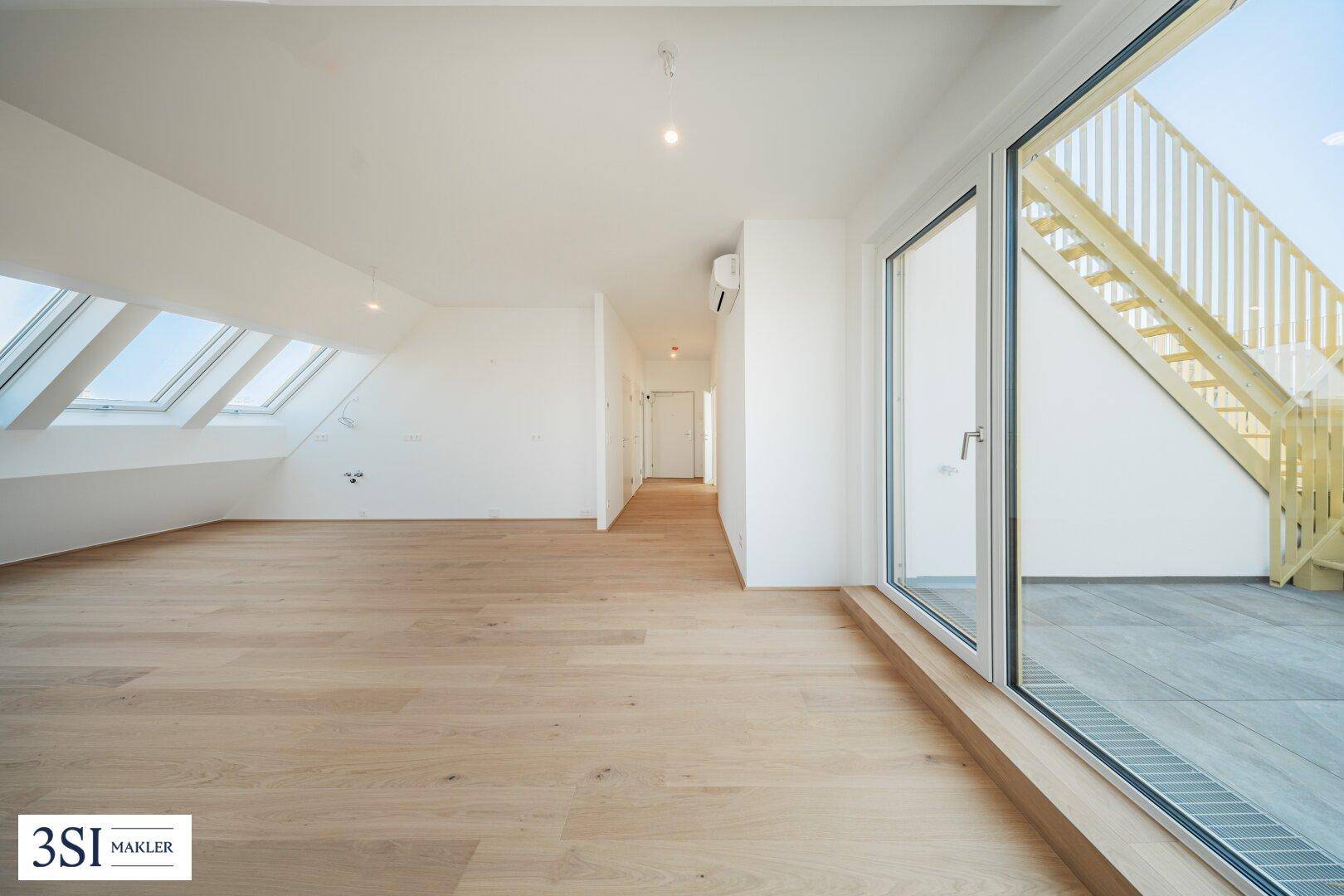 Helles Dachgeschosszimmer mit Holzboden, Dachfenstern und Zugang zu einer Außenterrasse.