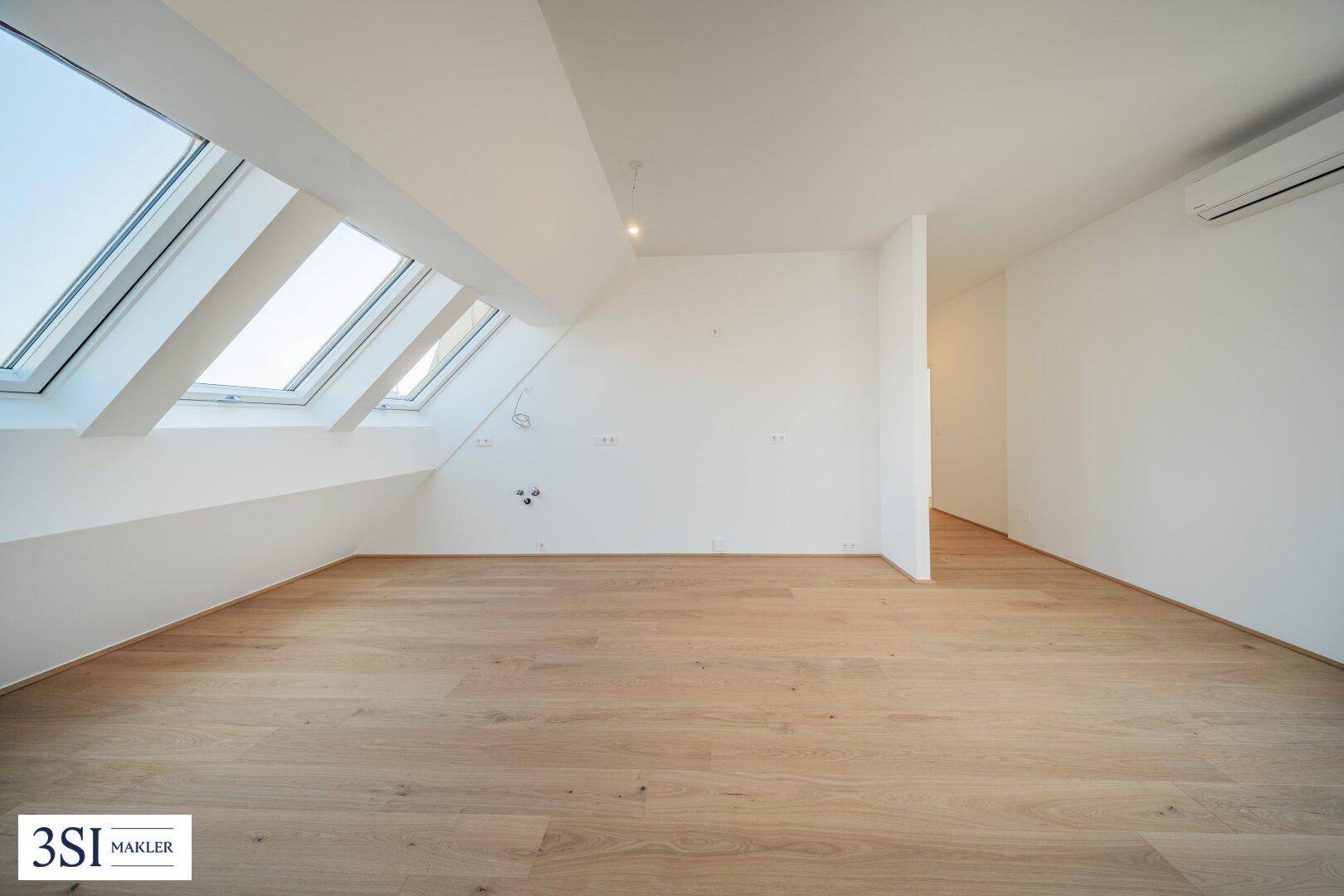 Heller Dachgeschossraum mit schrägen Wänden, Holzboden und mehreren Dachfenstern.
