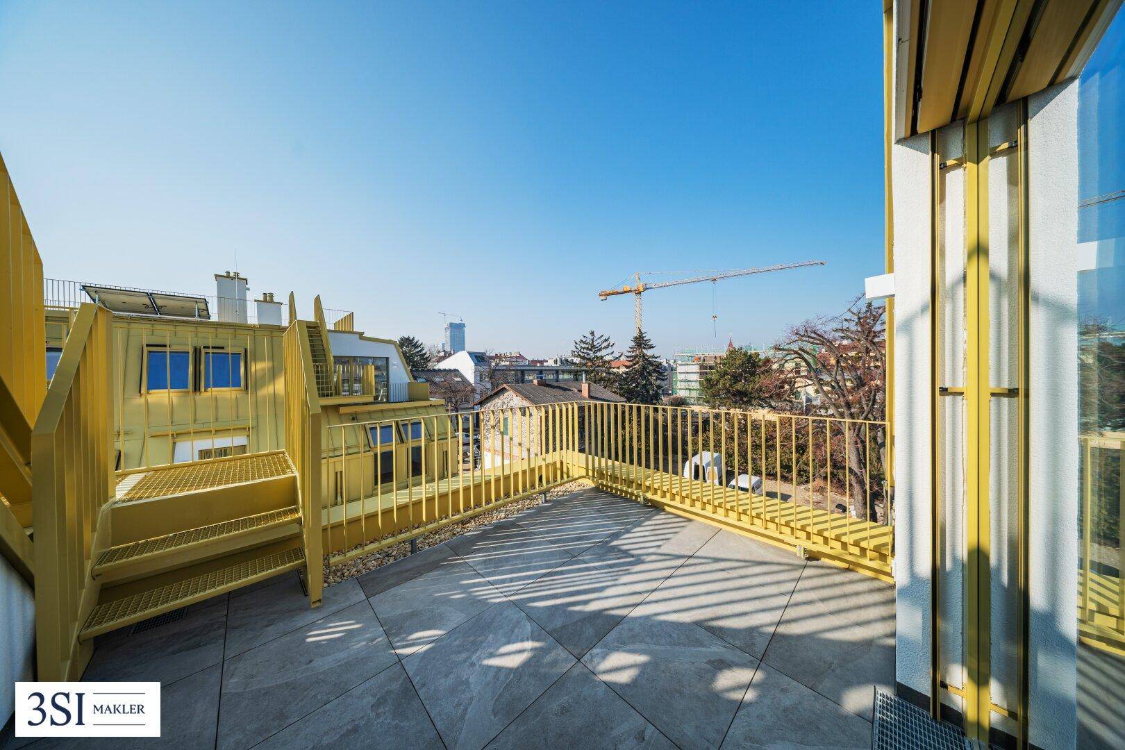 Sonniger Bereich der Dachterrasse mit gelbem Geländer und Blick auf die Stadt.