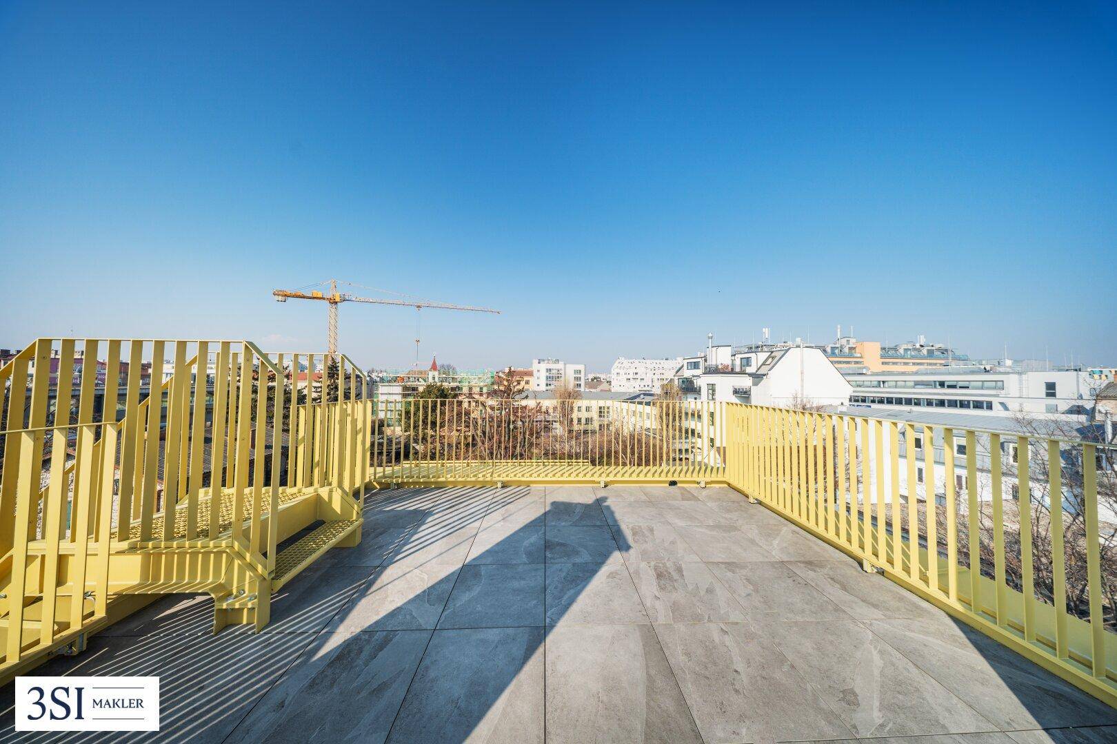 Geräumige Dachterrasse mit gelbem Geländer und weitem Blick über die Stadt.