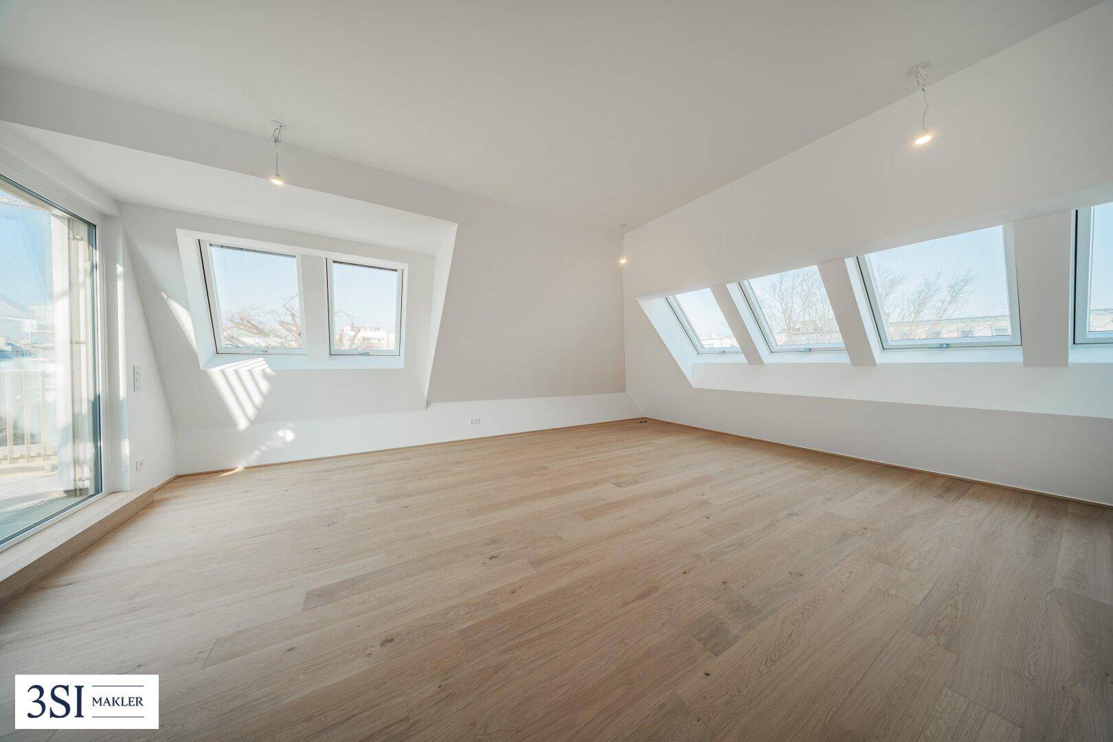 Geräumiger Dachgeschossraum mit Holzboden, großen Fenstern und Zugang zur Terrasse.