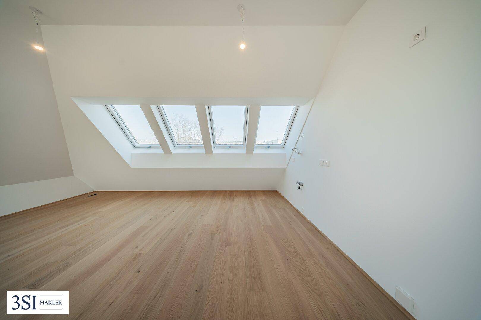 Lichtdurchfluteter Dachgeschossraum mit Holzboden und einer Reihe von Dachfenstern.
