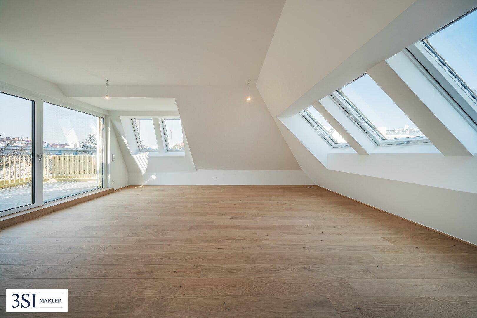 Geräumiger Dachgeschossraum mit Holzboden, großen Fenstern und Zugang zur Dachterrasse.