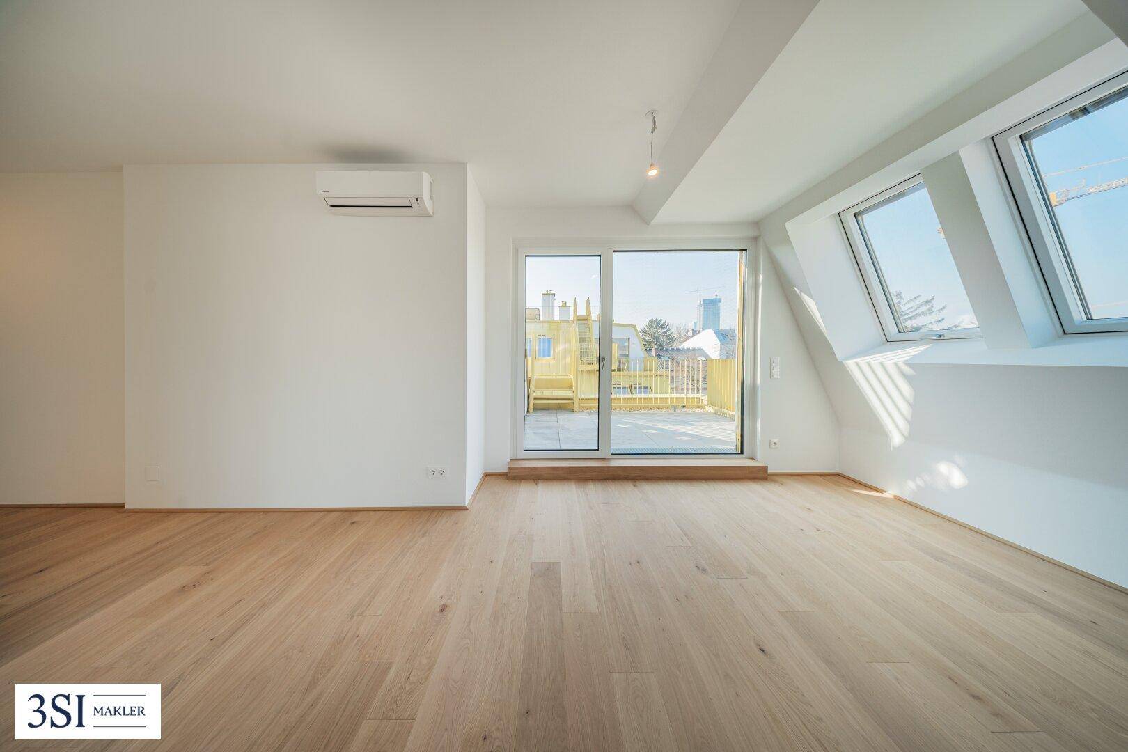 Lichtdurchfluteter Raum mit Holzboden, Dachfenstern und Zugang zur Dachterrasse.