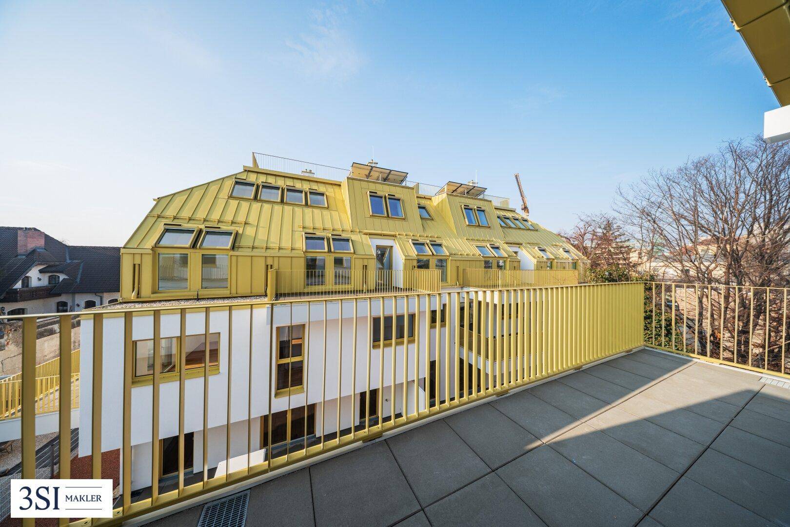 Große Dachterrasse mit gelbem Geländer und Blick auf das moderne Gebäude mit Mansarddach.