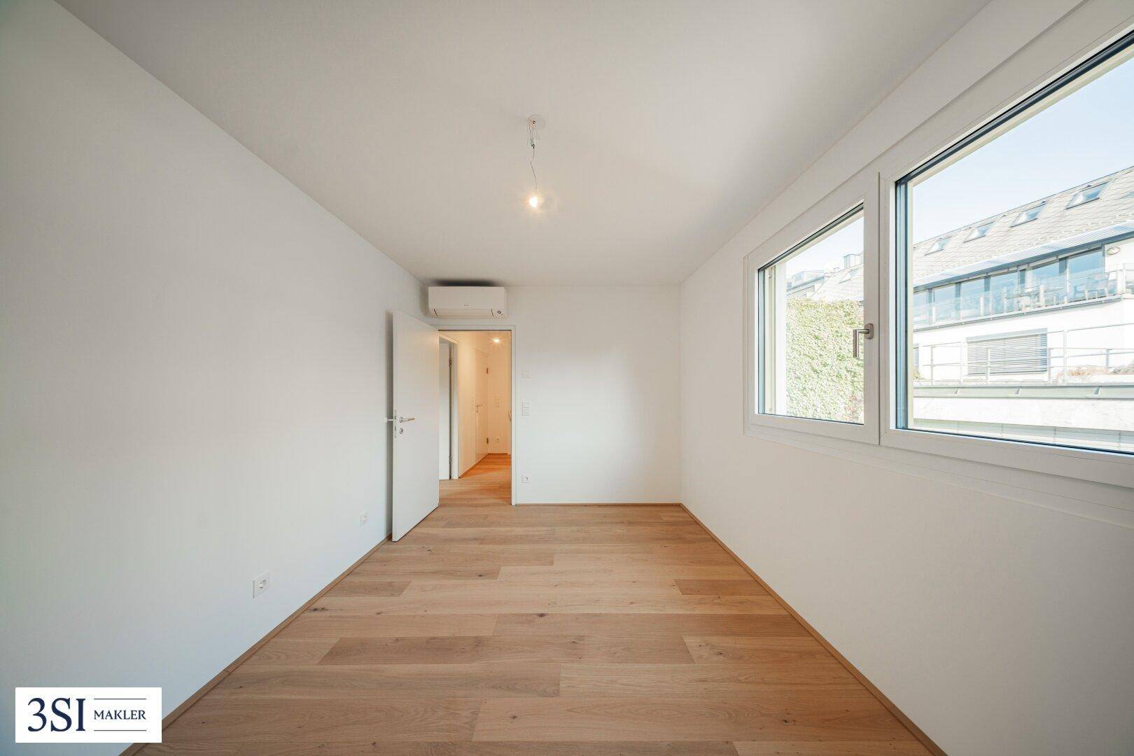 Helles Schlafzimmer mit Holzboden und Klimaanlage, bereit für die individuelle Einrichtung.