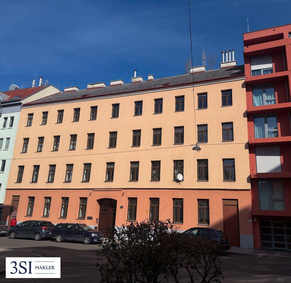 Historisches Wohngebäude mit orangefarbener Fassade und traditionellen Fenstern unter blauem Himmel.