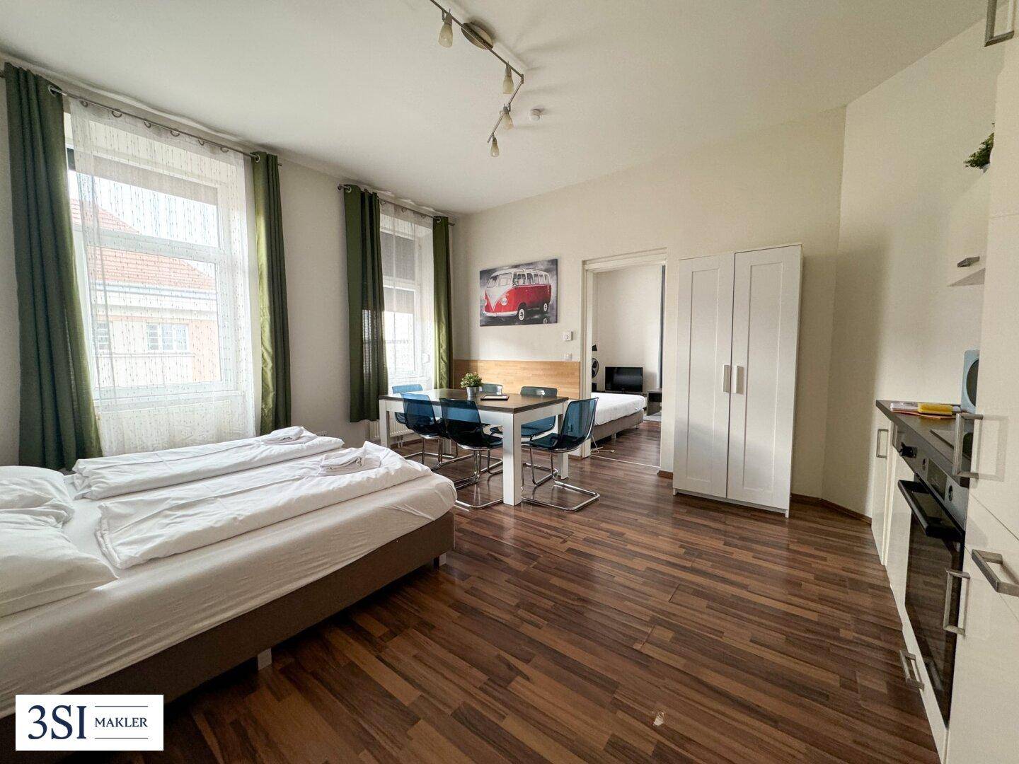 Helles Studio-Apartment mit Schlafbereich, Esstisch und kompakter Küchenzeile auf Holzboden.