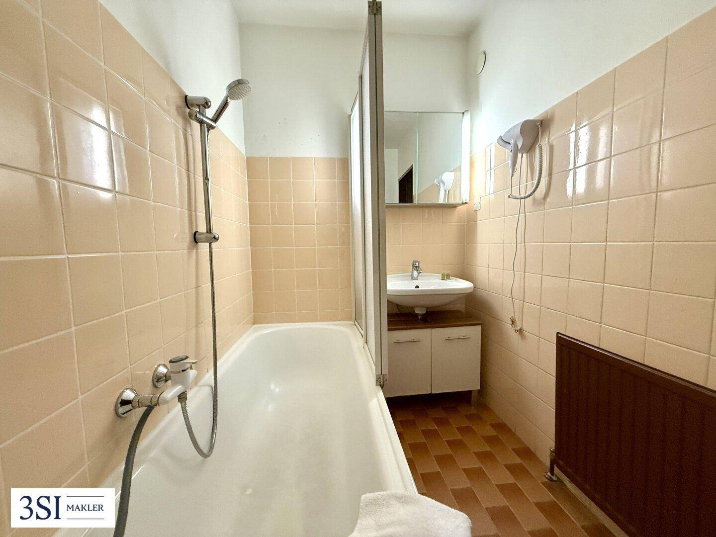 Badezimmer mit Badewanne, Duschvorrichtung und beigefarbenen Fliesen, ausgestattet mit einem Heizkörper.