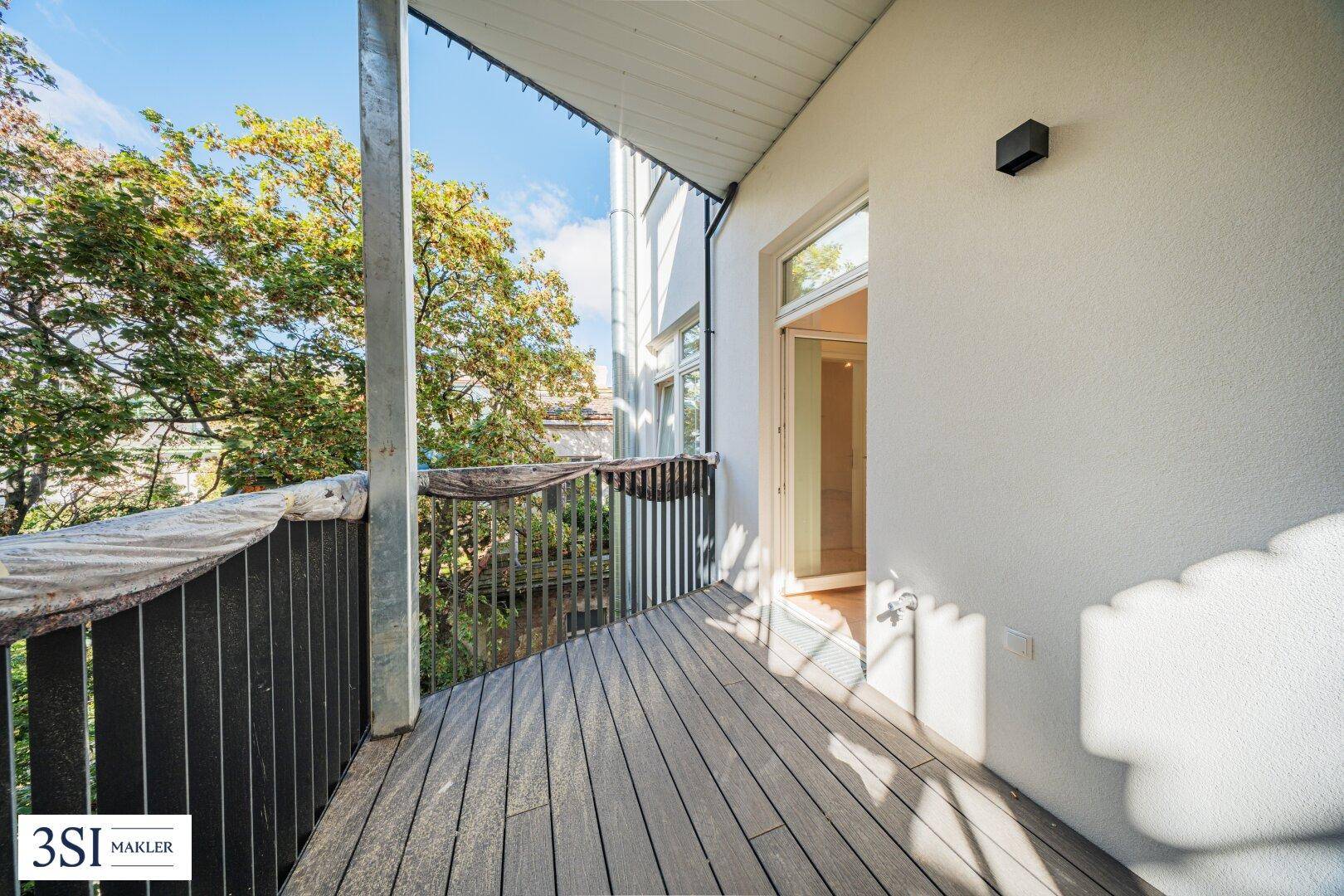 Kleiner Balkon mit Holzboden und Blick auf grüne Bäume.