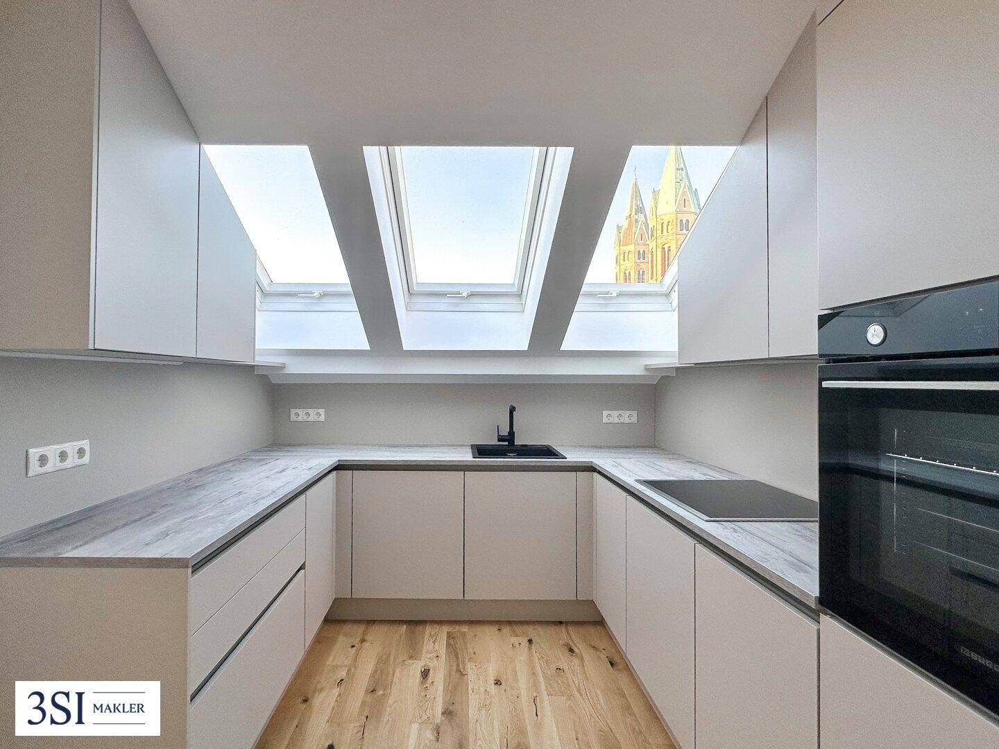 Moderne Küche mit Dachfenstern, Einbaugeräten und hellem Holzboden.