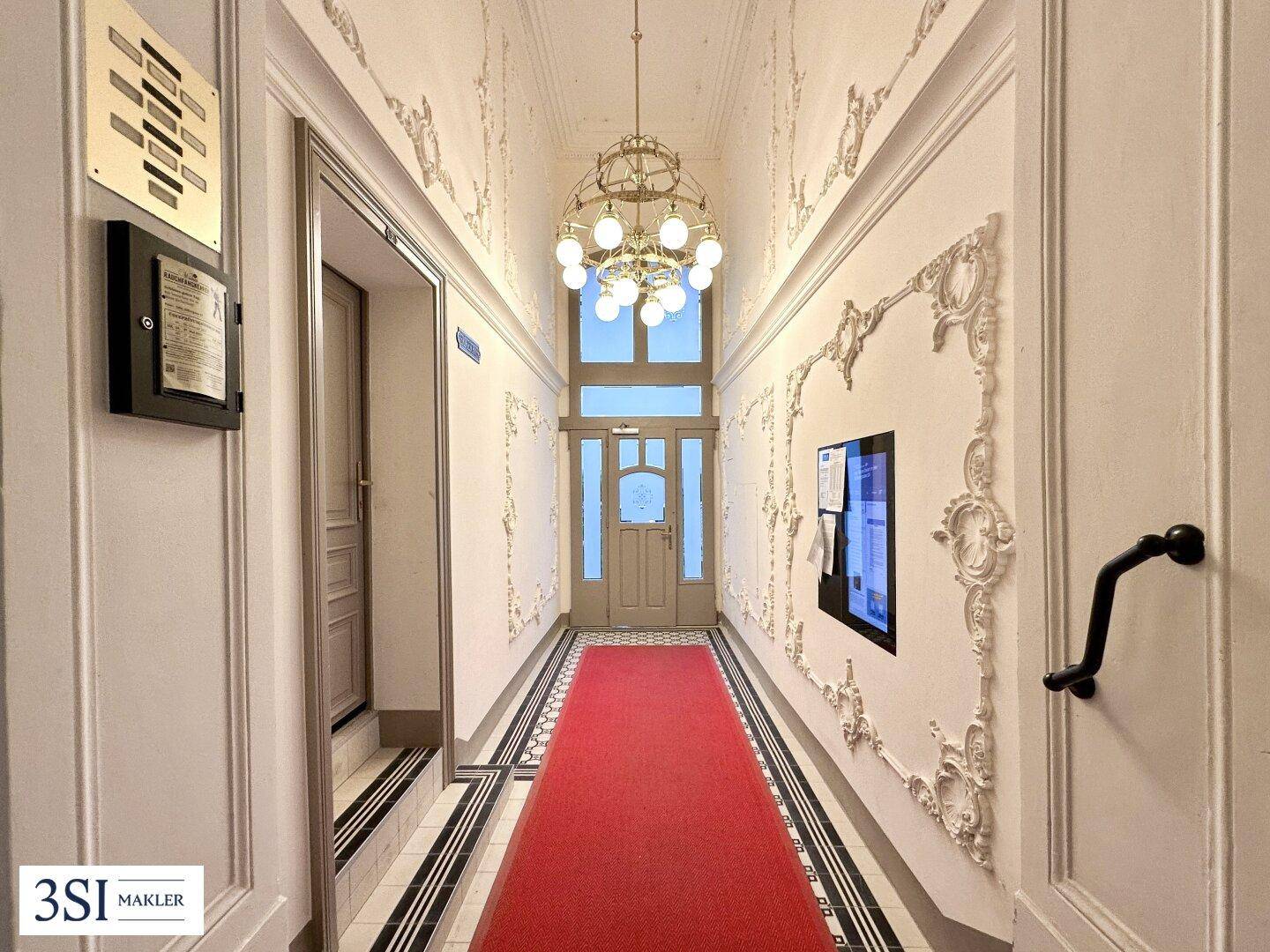 Eleganter Flur mit Stuckverzierungen, rotem Teppich und klassischer Beleuchtung.