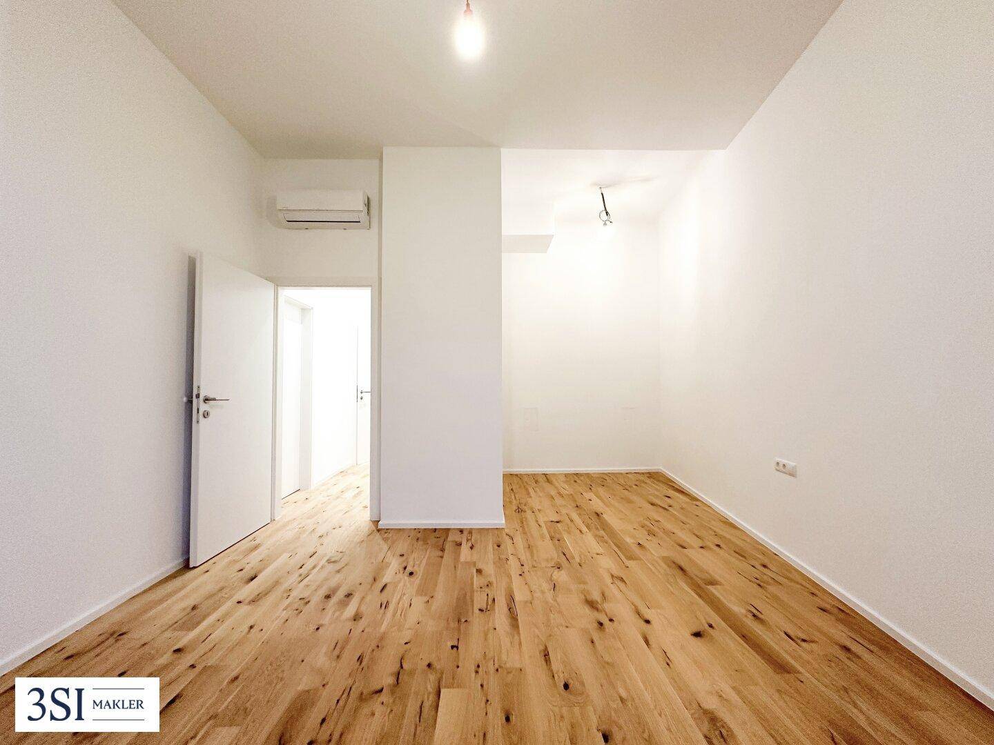 Helles Zimmer mit Holzboden, weiß gestrichenen Wänden und Klimaanlage.