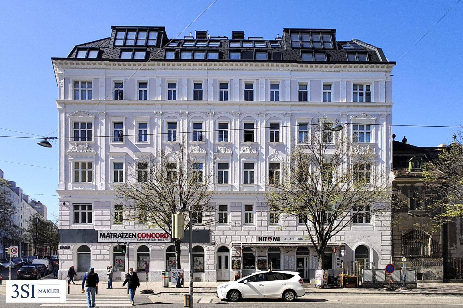 Historisches Mehrfamilienhaus mit klassischer Fassade, Geschäften im Erdgeschoss und modernem Dachausbau.