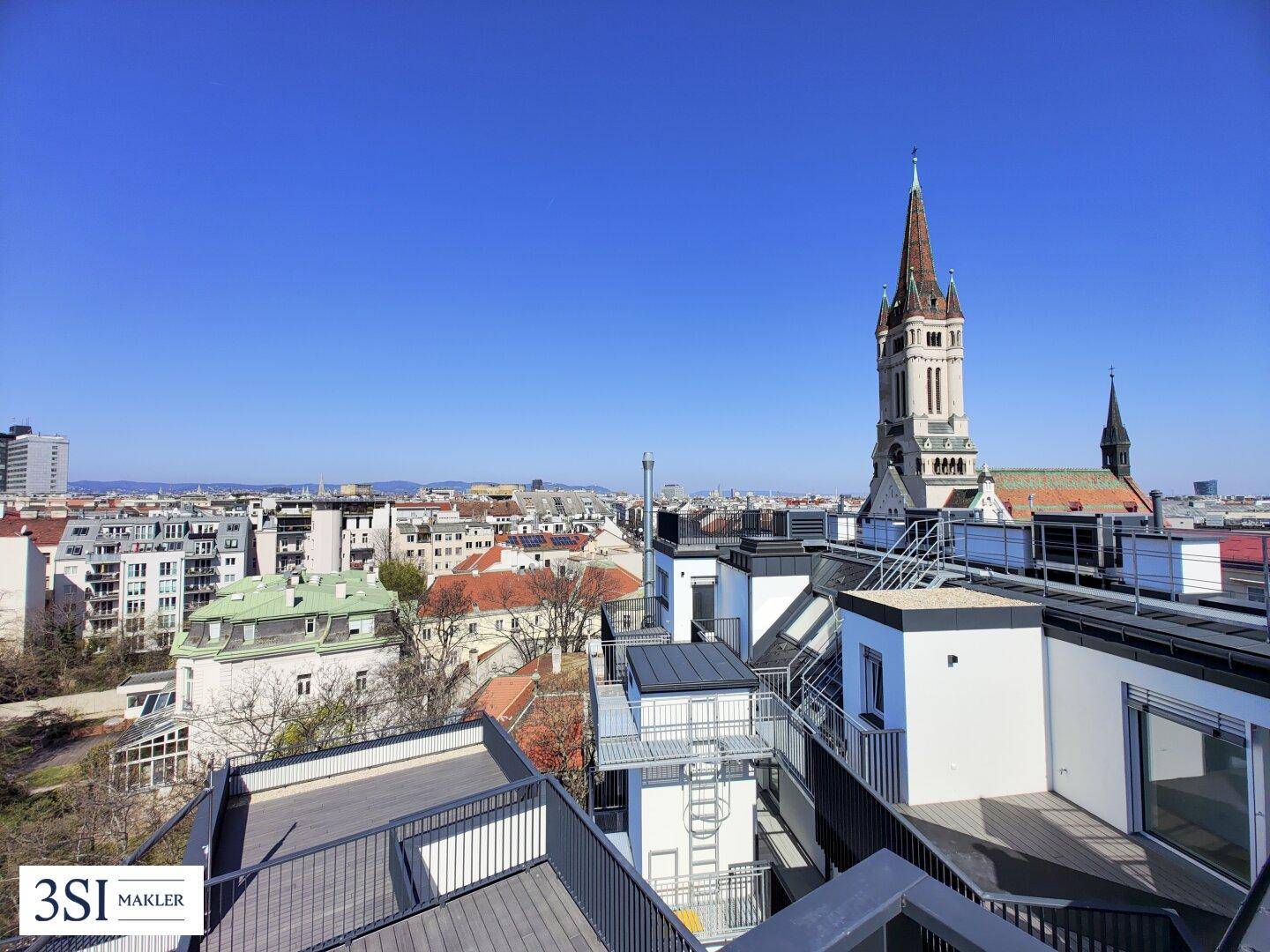 Weitläufiger Blick über die Stadt mit historischer Kirche und umliegenden Gebäuden von einer Dachterrasse.