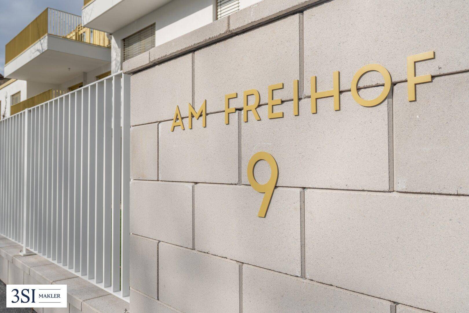 Detailansicht der Hausnummer und des Straßennamens an einer modernen Außenwand.