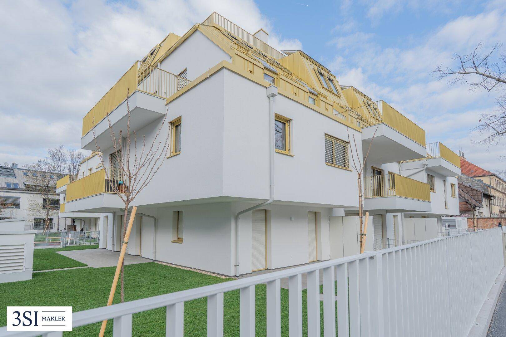 Modernes Mehrfamilienhaus mit weißer Fassade und gelben Akzenten unter einem bewölkten Himmel.