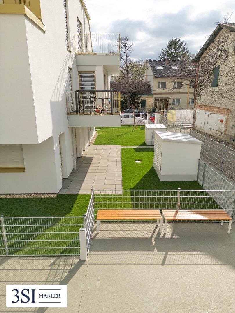 Blick von oben auf einen gemeinschaftlichen Gartenbereich mit Sitzbänken und Rasenflächen.