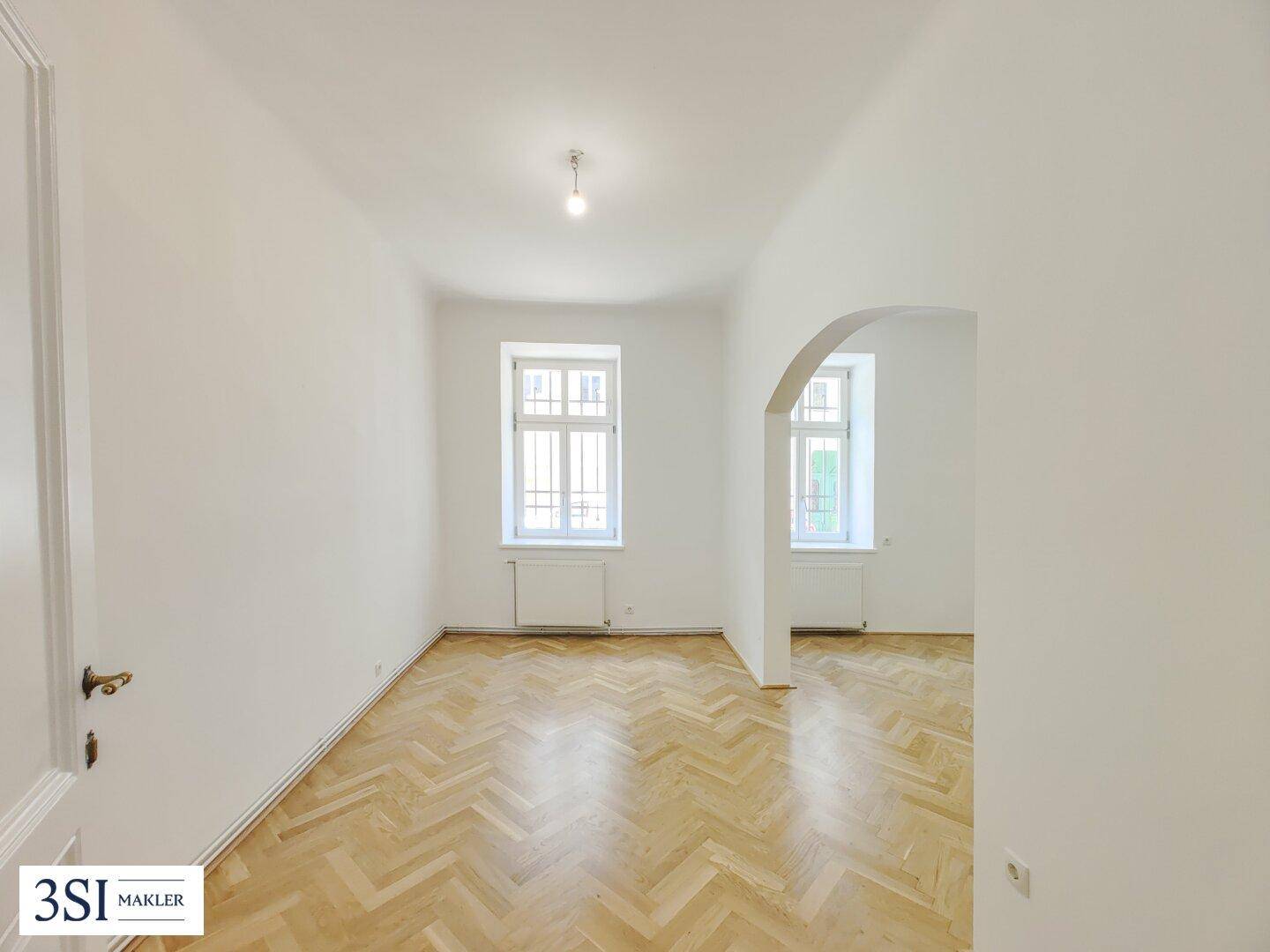 Lichtdurchfluteter Wohnraum mit elegantem Fischgrätparkett und klassischer Tür.