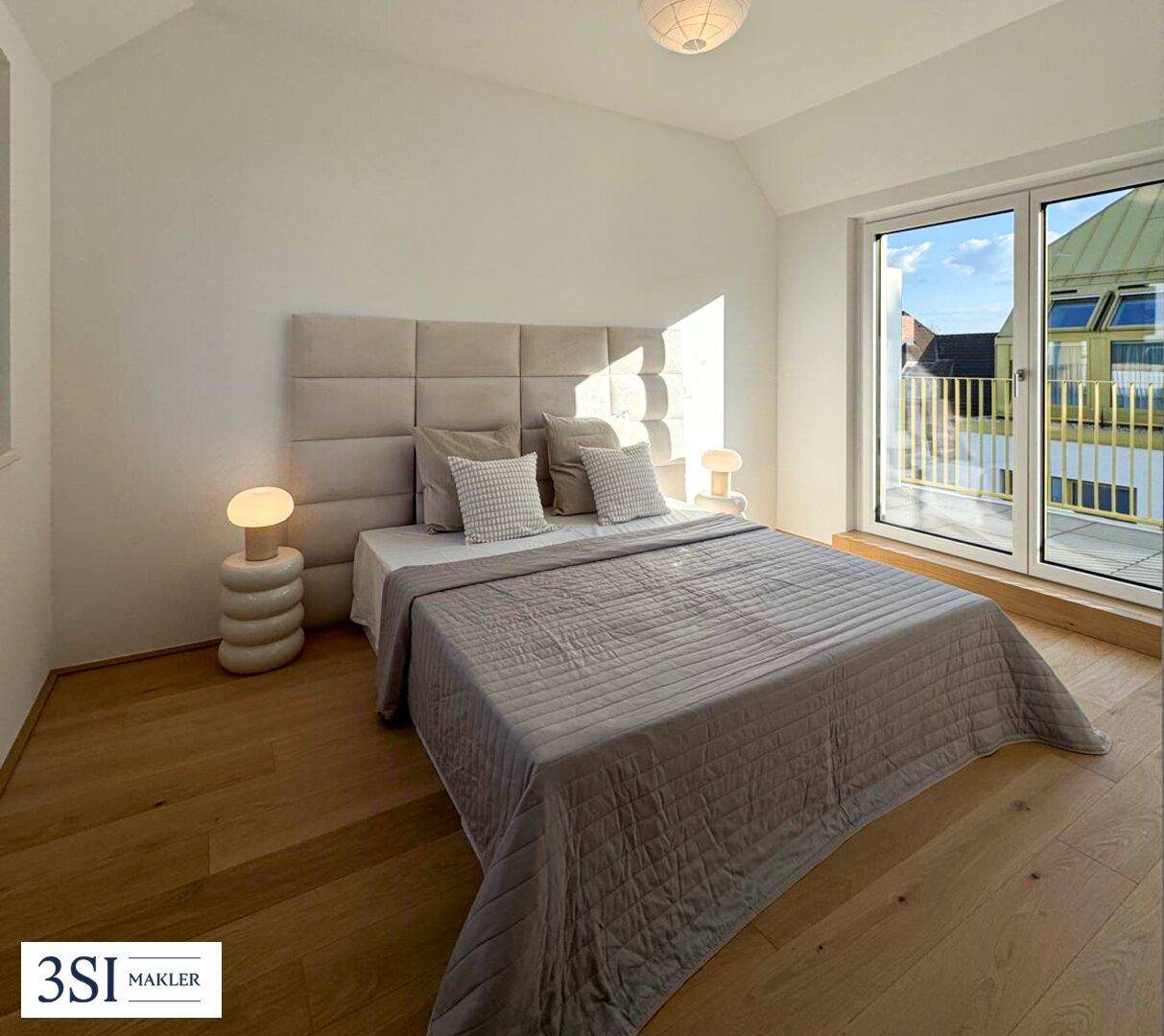 Helles Schlafzimmer mit Holzboden, gepolstertem Kopfteil und Zugang zu einem sonnigen Balkon.