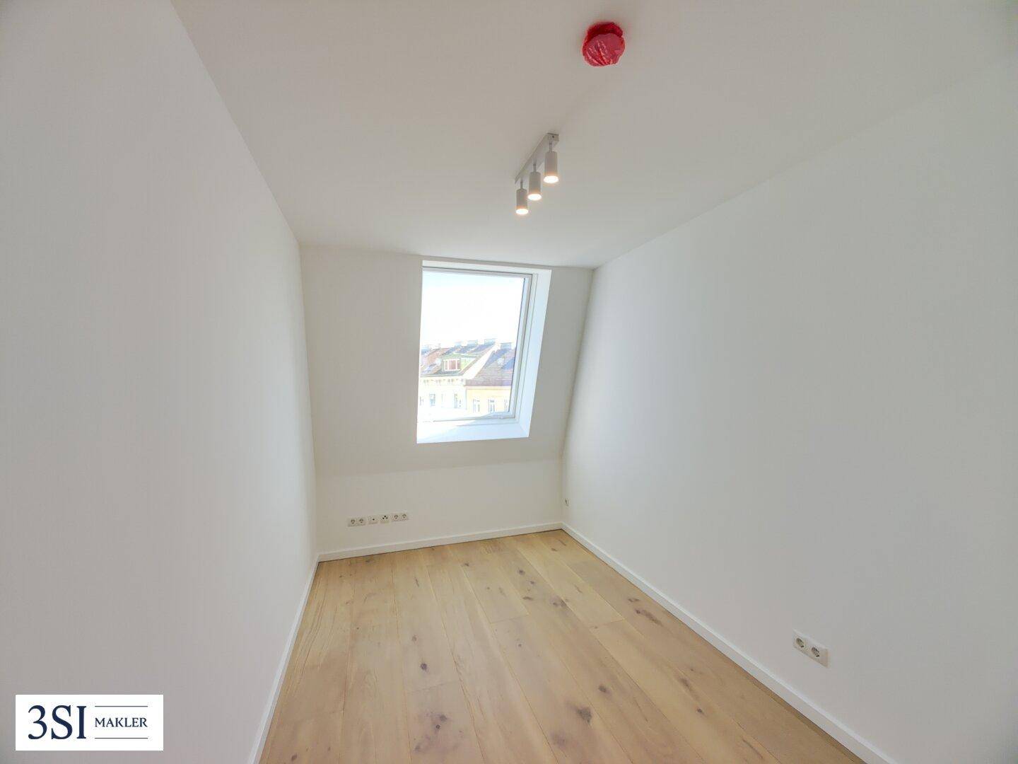 Kleines, helles Zimmer im Dachgeschoss mit Holzboden und einem einzelnen Dachfenster.