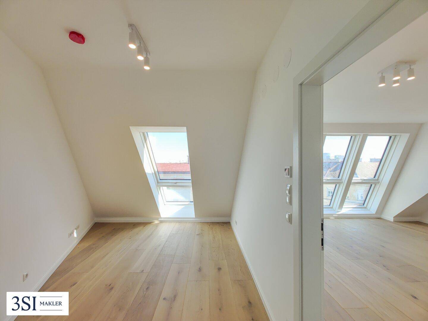 Helles Zimmer im Dachgeschoss mit Holzboden, schrägen Wänden und großen Dachfenstern.