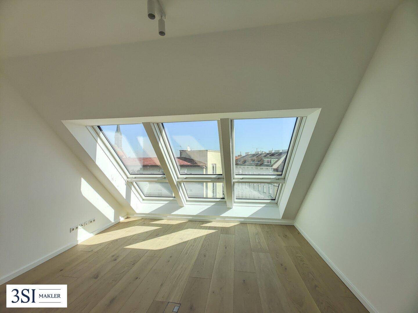 Lichtdurchflutetes Dachzimmer mit Holzboden und einer Reihe großer Dachfenster.