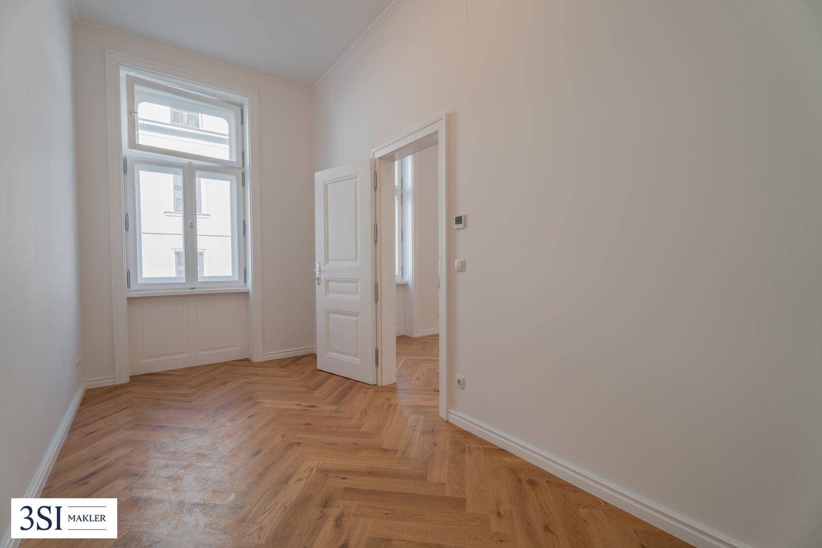 Lichtdurchflutetes Zimmer mit elegantem Fischgrätparkett und hohen Türen, ideal für Wohn- oder Schlafbereich.