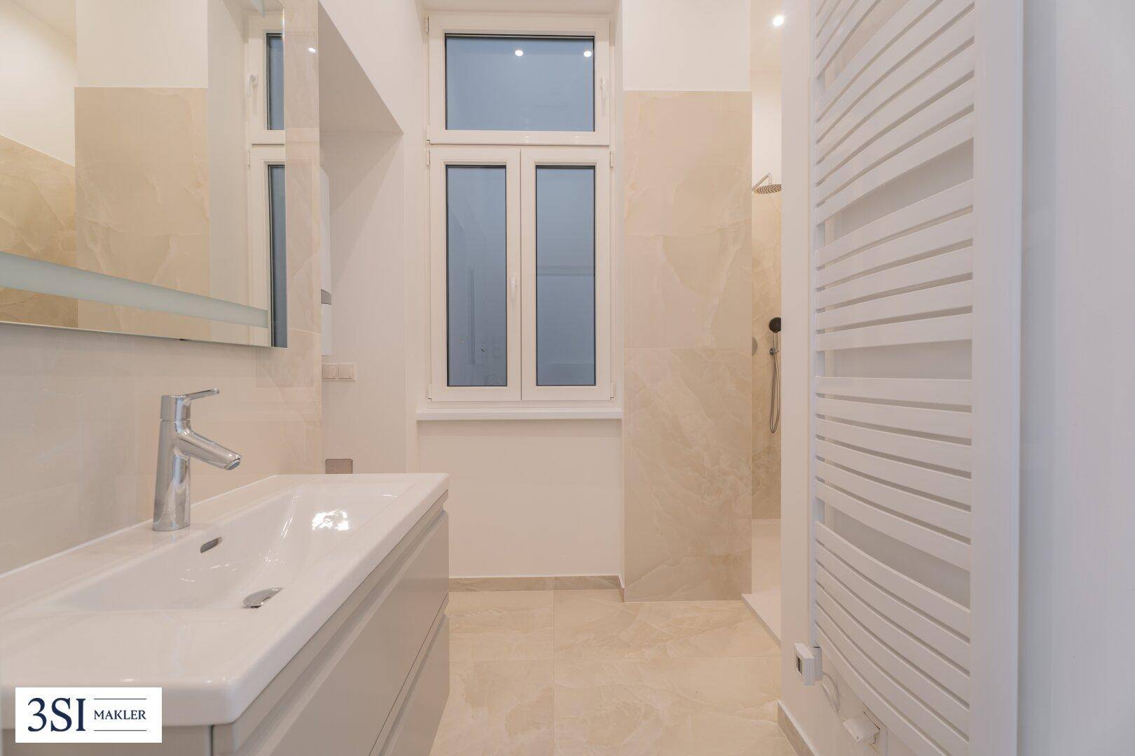 Modernes Badezimmer mit beigen Fliesen, Waschtisch und ebenerdiger Dusche sowie Fenster.