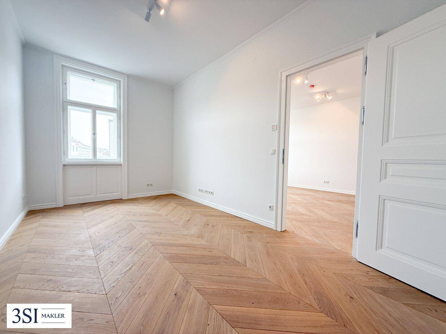 Geräumiges Zimmer mit Fischgrätparkett und Blick auf die umliegenden Gebäude.