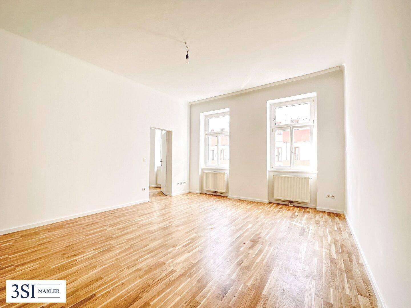 Großes, leeres Zimmer mit Holzboden und Fenstern, das vielseitig genutzt werden kann.