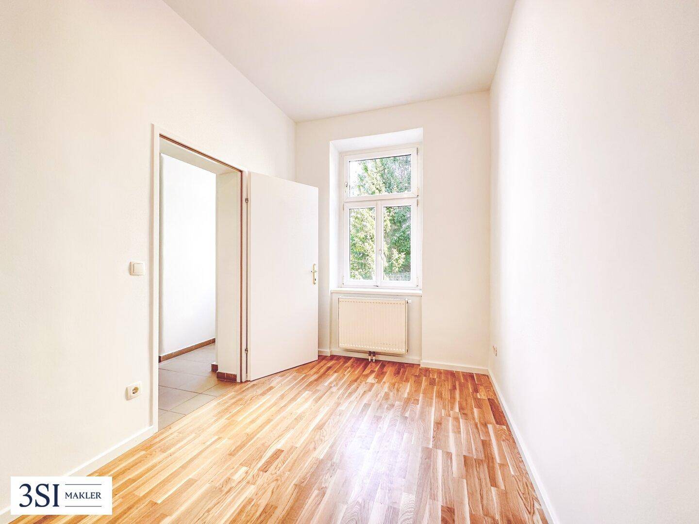 Leeres Zimmer mit Holzboden und Fenster, das sich gut als Kinder- oder Gästezimmer eignet.