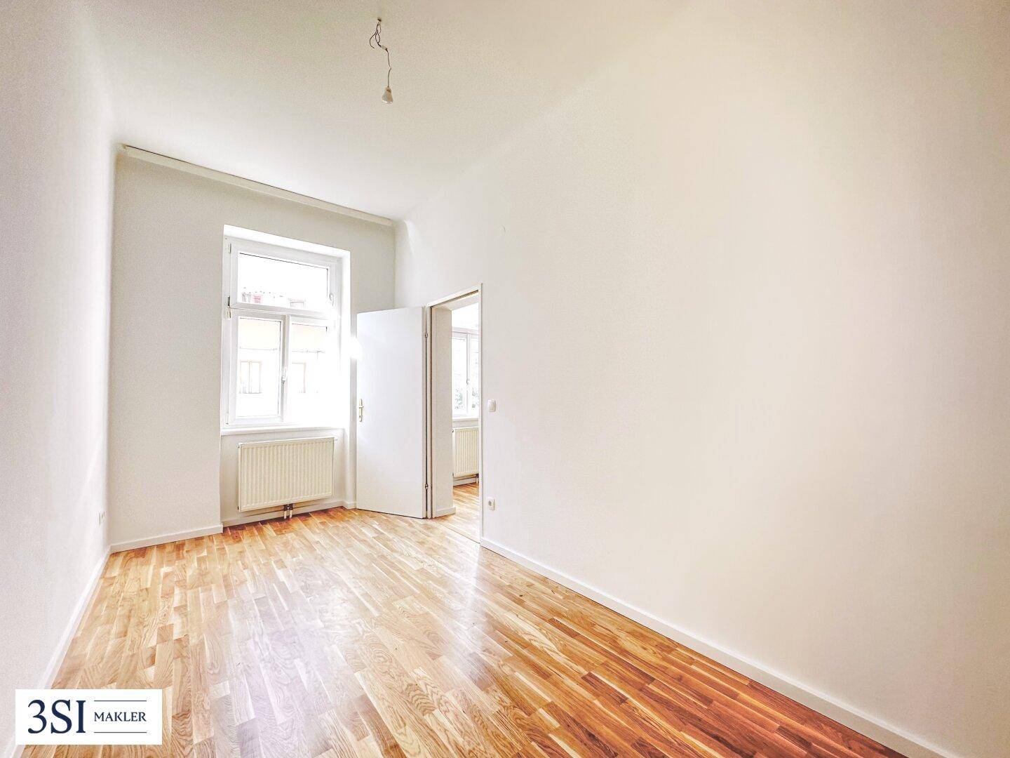 Helles, leeres Schlafzimmer mit Holzboden und einem Fenster, das viel Tageslicht bietet.