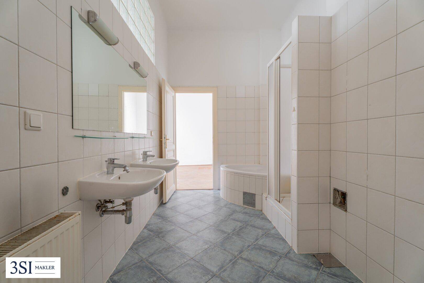 Badezimmer mit Doppelwaschbecken, Duschkabine und hellen Fliesen an Wänden und Boden.