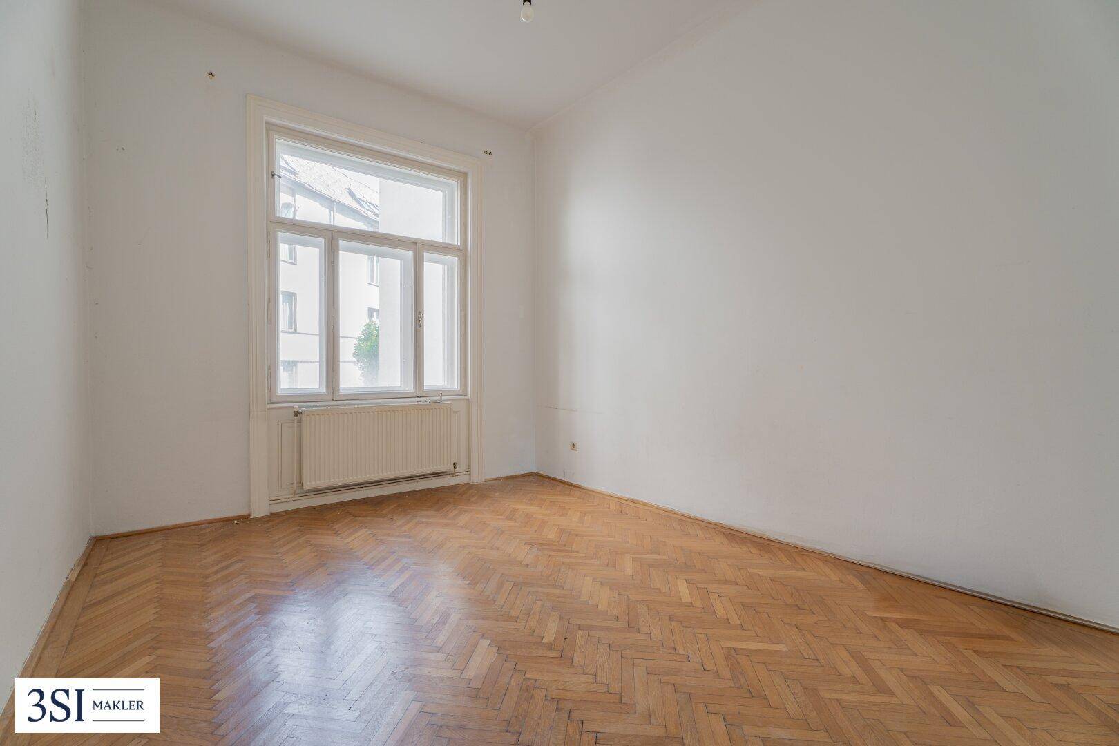 Helles Zimmer mit Fischgrätparkettboden, weißen Wänden und einem großen Fenster.