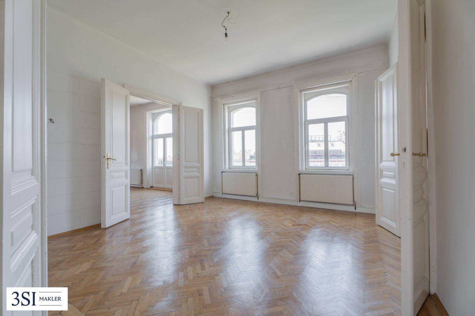 Helles Zimmer mit Fischgrätparkett, hohen Flügeltüren und viel Tageslicht.
