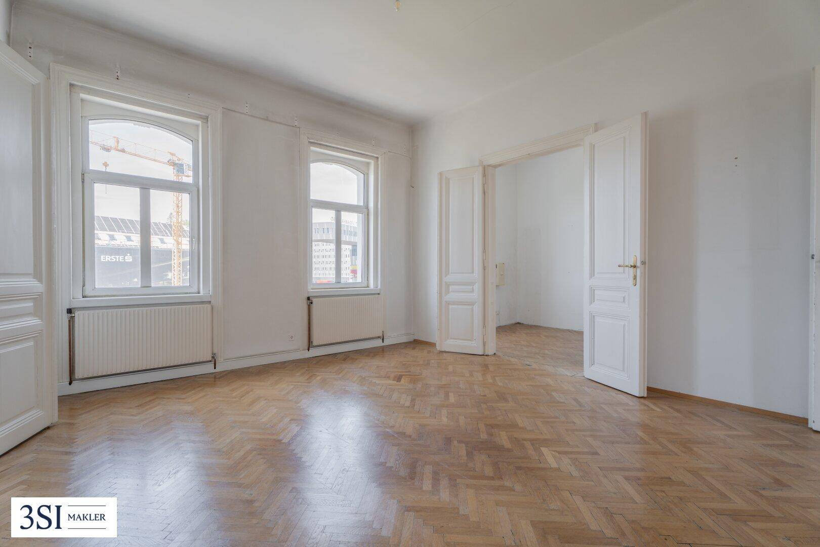 Großes Zimmer mit Fischgrätparkett, hohen Fenstern und Blick auf die Stadt.